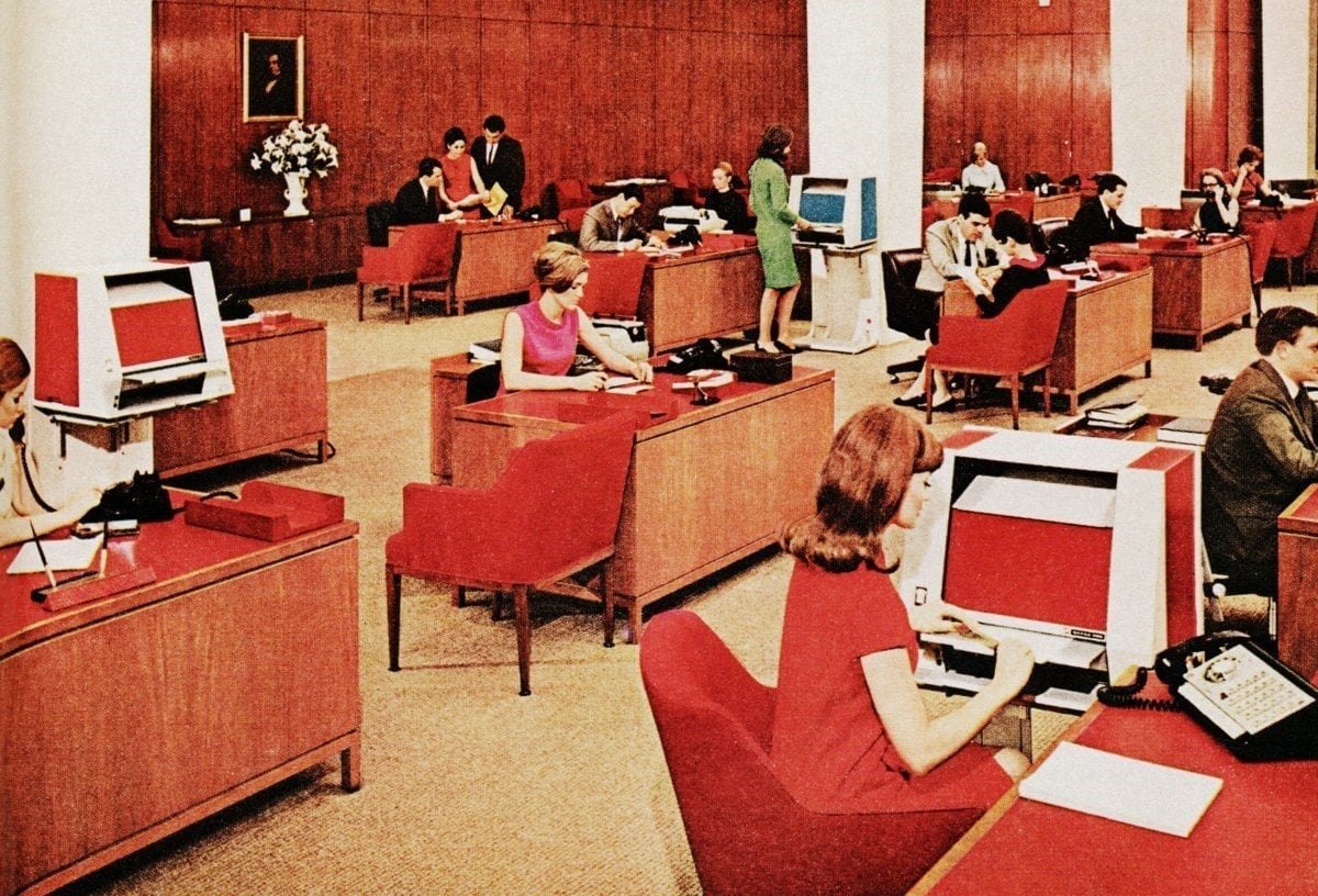 A 1960s open-plan office of terminals and red desks.